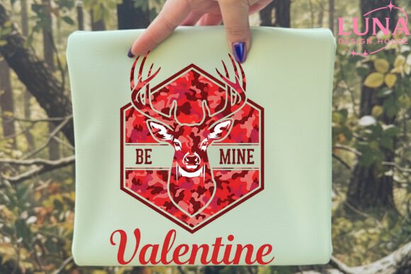 Laptop with a red deer design and 'Be Mine Valentine' text held by a hand in a forest setting.