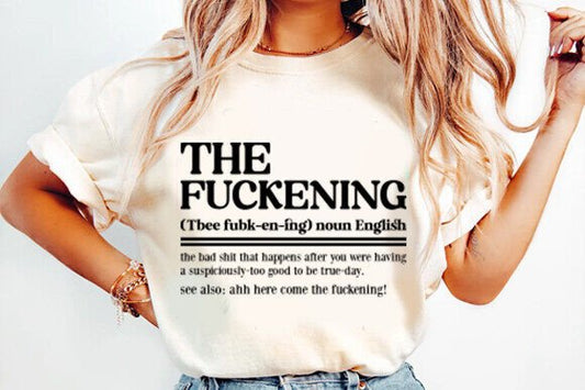 This image features a stylish woman sporting a light-colored t-shirt with the humorous and trendy phrase "The Fuckening" printed in bold, black lettering. The shirt, which is designed with a classic crew neck cut, provides a playful and edgy addition to her casual outfit.